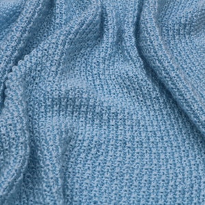 May include: A soft, light blue knitted blanket with a textured weave. The blanket is folded and draped over a white surface.