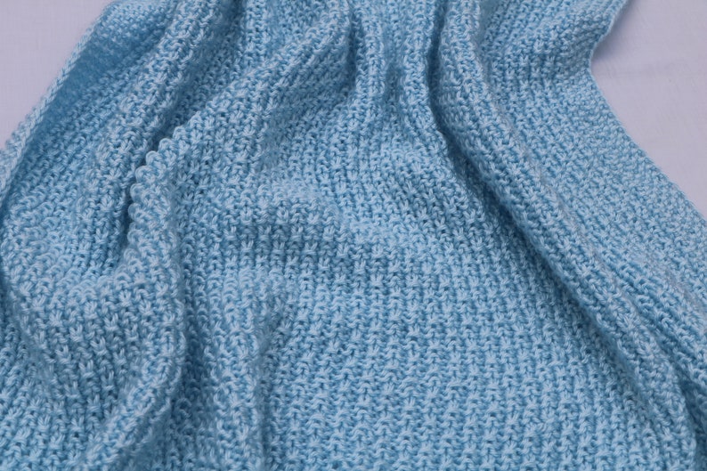May include: A soft, light blue knitted blanket with a textured weave. The blanket is folded and draped over a white surface.