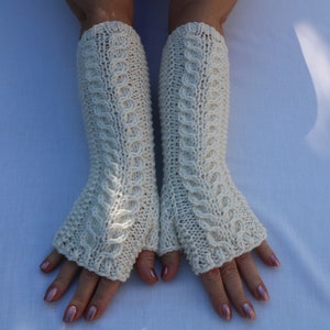 May include: A pair of white knitted fingerless gloves with a cable knit pattern.