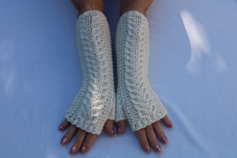 May include: A pair of white knitted fingerless gloves with a cable knit pattern.