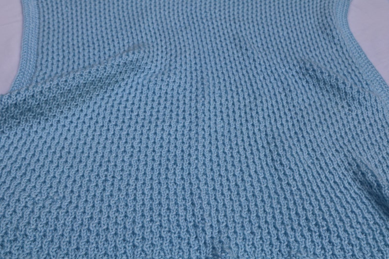 May include: A light blue knitted vest with a textured pattern.