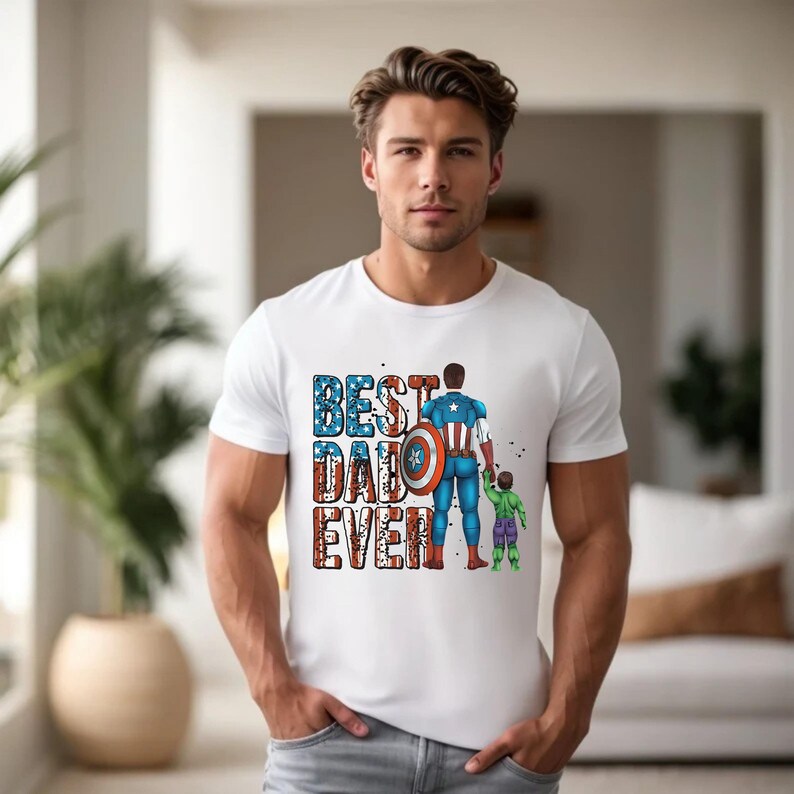 May include: White t-shirt with the text "BEST DAD EVER" in red, white, and blue. The graphic depicts a superhero with a shield and a child. The superhero is holding the child's hand. The shirt is short-sleeved.