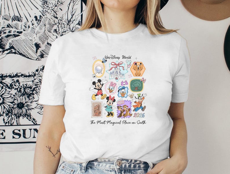 Peut inclure: T-shirt blanc orn&eacute; d'illustrations color&eacute;es de personnages et de lieux de Disney, dont Mickey Mouse, Minnie Mouse et le ch&acirc;teau de Cendrillon. Le texte "Walt Disney World" et "The Most Magical Place on Earth" sont &eacute;galement pr&eacute;sents.