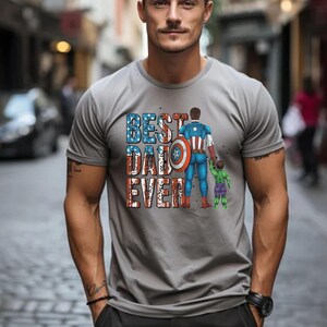 May include: Gray t-shirt with the text "BEST DAD EVER" in red, white, and blue. The graphic depicts a superhero and a child. The superhero is holding the child's hand.