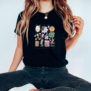 Peut inclure: T-shirt noir avec un motif color&eacute; repr&eacute;sentant divers personnages et ic&ocirc;nes Disney. Le design comprend le texte "Walt Disney World" et "2026". Le t-shirt a un col rond et des manches courtes.