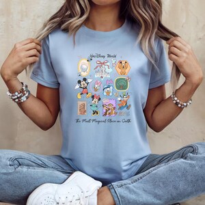 Peut inclure: T-shirt bleu clair orn&eacute; d'un motif color&eacute; de personnages et de lieux Disney. Le design comprend Mickey, Minnie, Donald et Dingo, avec le texte "Walt Disney World 2023" et "The Most Magical Place on Earth".
