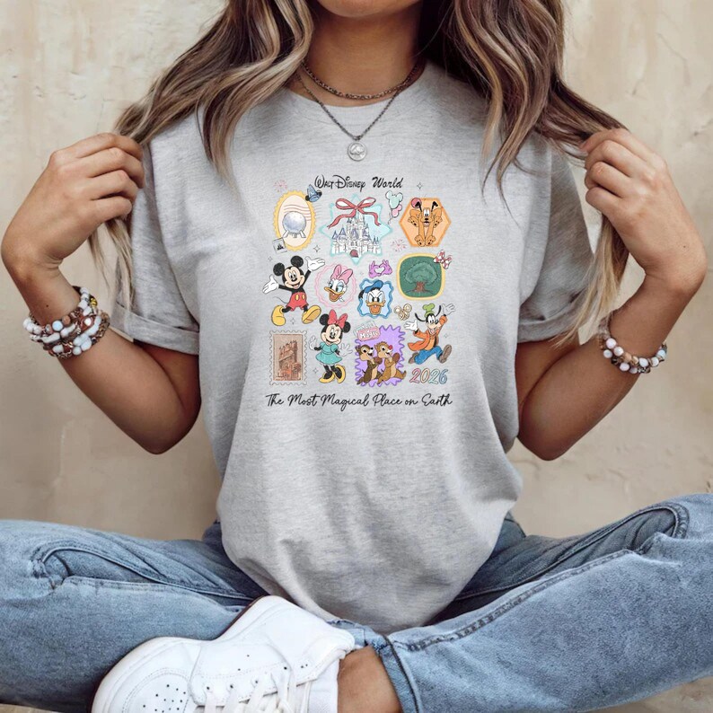 Peut inclure: T-shirt gris clair avec un motif graphique color&eacute; repr&eacute;sentant divers personnages et ic&ocirc;nes Disney. Le texte "Walt Disney World" et "The Most Magical Place on Earth" sont &eacute;galement visibles. Le t-shirt est en mati&egrave;re douce.