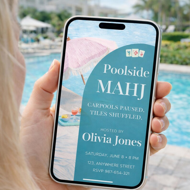 Op de afbeelding: Een smartphone toont een turquoise uitnodiging voor een Mahjong-evenement aan de rand van het zwembad. De uitnodiging bevat de tekst "Poolside MAHJ", "Hosted by Olivia Jones" en evenementdetails. Een roze en witte gestreepte parasol is zichtbaar.