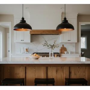 May include: A modern kitchen with a large island featuring a marble countertop and wooden base. Two black pendant lights hang above the island. A wooden range hood and white cabinets complete the design. A bowl of fruit and a vase of greenery add a touch of color.