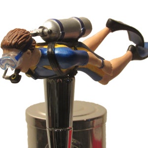 May include: A blue and yellow scuba diver figurine with a silver air tank, a black and blue diving mask, and black flippers. The figurine is mounted on a chrome beer tap.