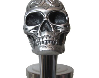 May include: Silver skull bottle stopper with a detailed design. The skull has a stylized design on the forehead and a detailed mouth.