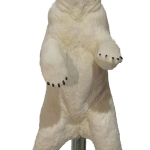 May include: A white polar bear figurine standing on a silver base. The bear is standing on its hind legs with its front paws raised. The bear has black eyes and a black nose.
