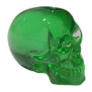 May include: A green glass skull figurine. The skull is detailed with eye sockets, a nose, and a mouth.