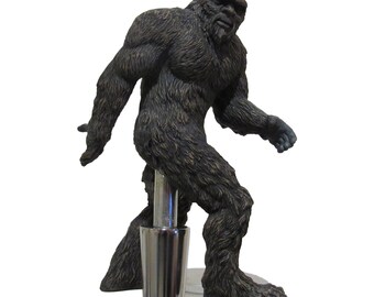 May include: A brown and black Bigfoot figurine beer tap handle. The Bigfoot is walking with its right foot forward and its left arm raised.