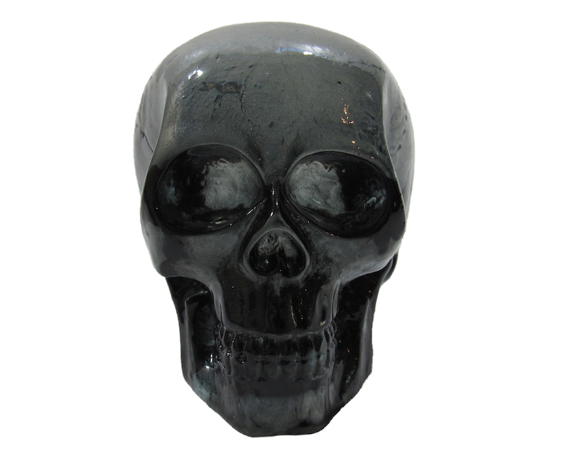 May include: A black skull figurine with a glossy finish. The skull has detailed features, including eye sockets, a nose, and a mouth.