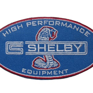 May include: A blue oval embroidered patch with the words "High Performance Shelby Equipment" and a white cobra logo.