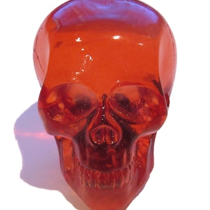 May include: A red glass skull with a detailed face and teeth. The skull is translucent and has a glossy finish.