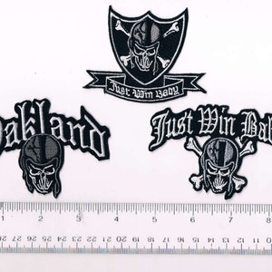 May include: Three black and white embroidered patches with a skull and crossbones design. The patches feature the text "Oakland", "Just Win Baby", and "Just Win Baby" with a shield.