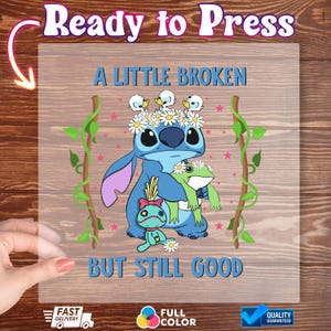 May include: A heat transfer vinyl sheet featuring a blue cartoon character with a daisy crown, holding a green frog. The text reads "A LITTLE BROKEN BUT STILL GOOD". Decorative vines and pink stars surround the characters. The sheet is held by a hand.