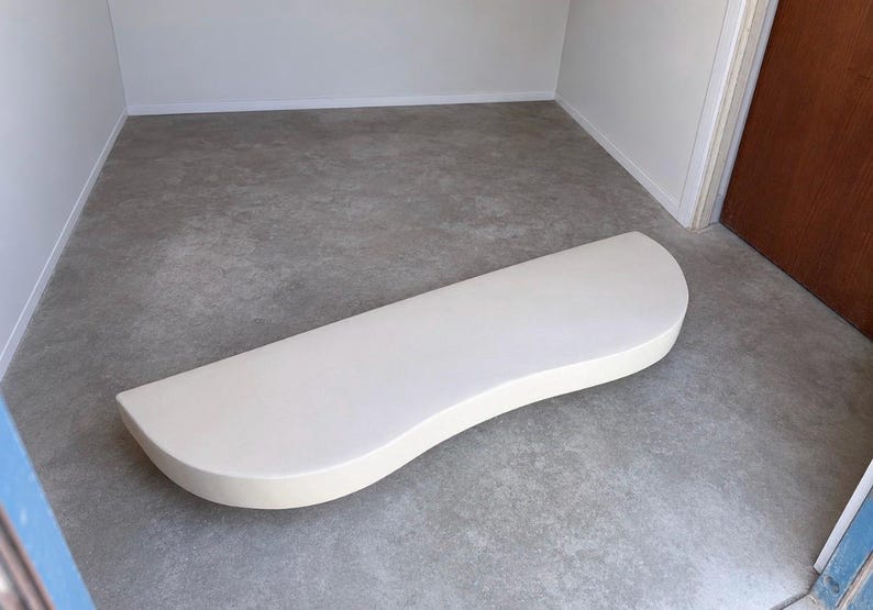 K&ouml;nnte beinhalten: Ein halbkreisf&ouml;rmiges, cremewei&szlig;es Schaumstoffpolster mit einer glatten, matten Oberfl&auml;che und einer geschwungenen Vorderkante. Das Objekt hat eine dicke, solide Konstruktion mit einer flachen Oberseite und einem abgerundeten Profil.