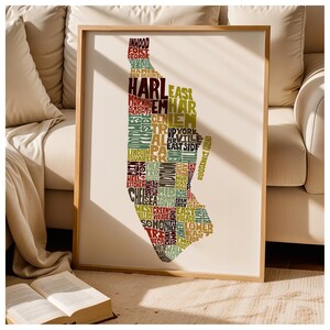 May include: A framed wall art print featuring a typographic map of Manhattan, New York. The map is composed of neighborhood names in various colors including red, green, brown, and yellow, arranged to form the shape of the island of Manhattan.