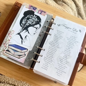 May include: A ring-bound planner featuring a page titled Trigger List for your planner with a list of categories. The adjacent page displays a black and white illustration of a person with bookshelves in their hair and a stack of three books below.