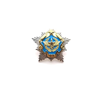 Puede incluir: Una insignia militar detallada en forma de estrella con un emblema central azul y dorado. La insignia presenta una estrella dorada en la parte superior y un diseño detallado dentro del centro azul. Los bordes exteriores tienen un diseño plateado en forma de sol.
