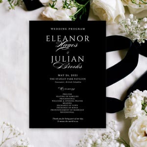 Könnte beinhalten: Eine rechteckige schwarze Hochzeitskarten-Programmkarte mit weißer Serifenschrift und Schreibschrift. Der Text lautet: WEDDING PROGRAM, ELEANOR Hayes & JULIAN Brooks, MAY 24, 2025, THE STANLEY PARK PAVILION, Vancouver, British Columbia, CEREMONY, PRELUDE, SEATING OF FAMILIES, PROCESSIONAL, WELCOME & OPENING PRAYER, READING, EXCHANGE OF VOWS, EXCHANGE OF RINGS, PRONOUNCEMENT OF MARRIAGE, RECESSIONAL, Thank you for being part of our day. It means the world to us.