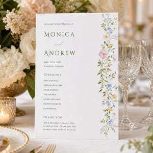 May include: A wedding program with floral accents. The program features the names "Monica and Andrew", the date May 12th, 2027, and the location Toronto, Canada. The program has a floral border with pink, blue, and yellow flowers.