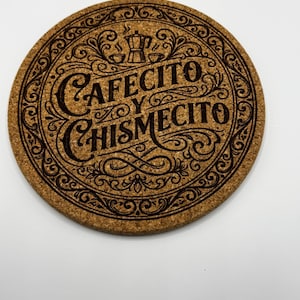 May include: Round cork coaster with the words "Cafecito y Chismecito" in a decorative font. The coaster features a coffee pot and cup design, with an ornate border. The coaster is brown with dark brown etched details.