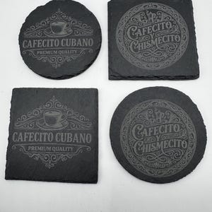 May include: Four dark gray slate coasters. Two are round and two are square. Each coaster features etched text and designs. The text on two coasters reads "CAFECITO CUBANO PREMIUM QUALITY". The other two read "CAFECITO Y CHISMECITO".