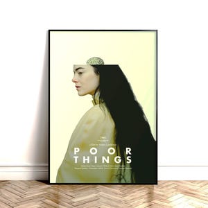 May include: A framed movie poster for Poor Things featuring a profile view of a person with long black hair and a pale yellow background. A small brain illustration sits atop the head. The text reads Poor Things and lists the film credits.