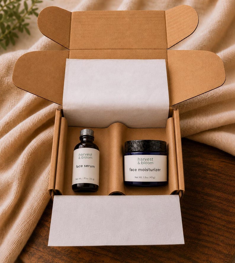 May include: A brown cardboard gift box containing a small glass bottle of Harvest & Bloom face serum with a 1 fl oz (30 g) label and a dark blue jar of Harvest & Bloom face moisturizer with a 1.5 oz (43 g) label, both nestled in a custom insert.