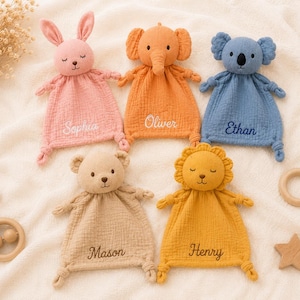 Könnte beinhalten: Fünf personalisierte Baby-Schmusetücher in Rosa, Orange, Blau, Beige und Gelb, jeweils in Tierform. Die Namen "Sophia", "Oliver", "Ethan", "Mason" und "Henry" sind aufgestickt. Ein Holzrassel, ein Ring und ein Stern sind ebenfalls zu sehen.