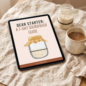 Könnte beinhalten: Ein digitales Tablet zeigt "DEAR STARTER: A 7-DAY SOURDOUGH GUIDE" mit einer Gläser-Illustration. Daneben befinden sich ein Glas mit schwarzem Band und eine Kaffeetasse. Die Gegenstände liegen auf einer beigen Leinenoberfläche, mit Mehl verstreut.