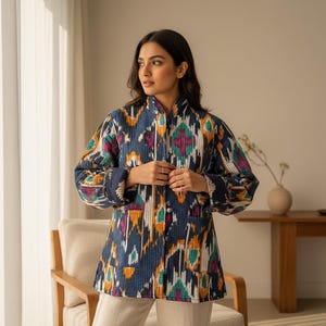 May include: A quilted jacket with a vibrant, geometric pattern in shades of blue, orange, pink, and green. The jacket has a mandarin collar, button-up front, and two front pockets. The sleeves are long and the jacket is worn over white pants.