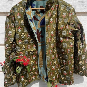 Puede incluir: Una chaqueta reversible con exterior verde oliva y un patr&oacute;n floral repetitivo en rojo, blanco y amarillo. El forro interior es de tela azul claro adornada con grandes y llamativos motivos florales y de hojas bordados en azul oscuro, marr&oacute;n y dorado.