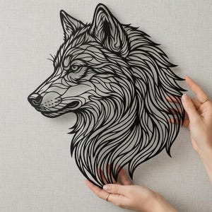 Könnte beinhalten: Ein schwarzes, lasergeschnittenes Wandkunstwerk mit einem Wolfskopf. Das Kunstwerk zeigt komplizierte Linien, die das Profil des Wolfes mit einer detaillierten Mähne und einem fokussierten Blick darstellen. Das Stück wird von zwei Händen gehalten.