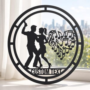 May include: A circular black wall art piece featuring a silhouette of a couple dancing. To the right, a heart shape is formed by various musical notes. The words CUSTOM TEXT are cut out at the bottom of the circular frame, which has a border.