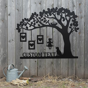 Könnte beinhalten: Schwarze Metallbaum-Silhouette mit Schaukel, Mädchen und Hund. Der Baum hat hängende Rahmen mit Herzen und ein Nest. Der Text "CUSTOM TEXT" steht unter dem Baum. Eine Gießkanne, Handschuhe und eine Schaufel befinden sich im Vordergrund.