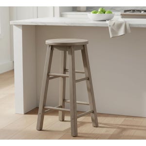 May include: A light gray wooden bar stool with a round seat and four legs. The stool has two horizontal supports between the legs for added stability. The stool is positioned in front of a white countertop.