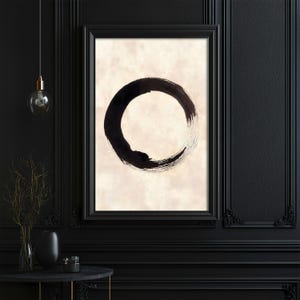 Op de afbeelding: Een ingelijst kunstwerk met een grote, abstracte zwarte cirkel op een beige achtergrond. Het kunstwerk wordt tentoongesteld op een zwarte muur, wat een minimalistische esthetiek creëert. De afbeelding is een close-up van het kunstwerk.