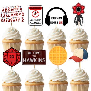 May include: Cupcakes with white frosting and themed toppers. Toppers include a red die, a sign that says "Welcome to Hawkins", a waffle, a baseball cap, and a Demogorgon. Other toppers have text that says "Friends Don't Lie" and "Demogorgons Are Not Allowed".