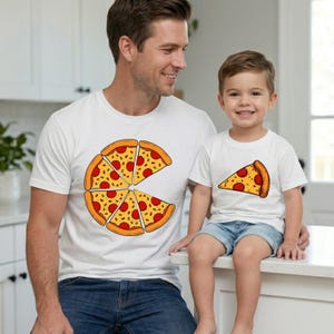 May include: White t-shirts with pizza slice designs. One shirt features a pizza with several slices, while the other has a single slice. The pizza has red pepperoni and yellow cheese on a brown crust.