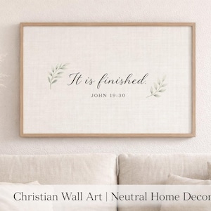 May include: Framed wall art with the text "It is finished" and the reference "John 19:30". The artwork features a light beige background with a linen texture, a wooden frame, and delicate green leaf accents. The overall theme is Christian wall art.