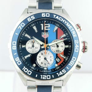 Op de afbeelding: Een TAG Heuer Formula 1 horloge van roestvrij staal met een blauwe, rode en witte wijzerplaat. Het horloge heeft een tachymeter bezel en een bijpassende blauwe en zilveren band. De wijzerplaat toont meerdere sub-wijzerplaten en het nummer 12.