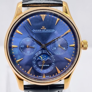 May include: A gold-toned Jaeger-LeCoultre wristwatch with a blue face and black leather band. The watch face features multiple sub-dials, gold markers, and the text "AUTOMATIQUE" and "SWISS MADE".