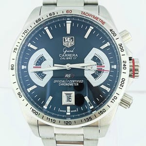 Op de afbeelding: Een roestvrijstalen TAG Heuer Grand Carrera Calibre 17 horloge met een donkerblauwe wijzerplaat. Het horloge heeft een tachymeterschaal, chronograaf sub-wijzerplaten en een datumvenster op 4 uur. De armband is van roestvrij staal.