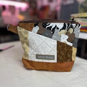 Op de afbeelding: Een patchwork stoffen etui met een bruine rits en een kleine lusgreep. De etui heeft verschillende stofpatronen, waaronder bloemen-, geometrische en dierenprints. Het label luidt "Junco Studio".