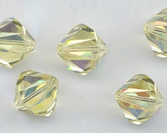 May include: Five iridescent yellow crystal beads with a faceted design. The beads are small and have a square shape.